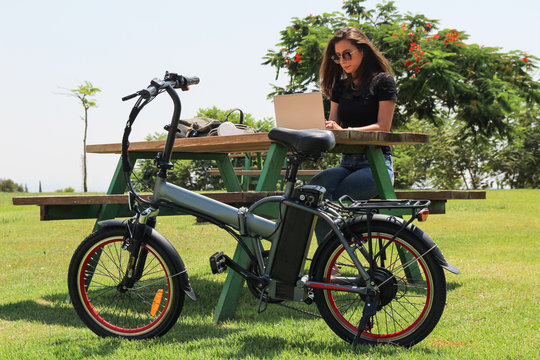 Women with electric Bicycle and laptop sitting in the park