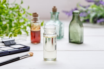 Glass small bottle with liquid in it and cosmetics on a white wooden table
