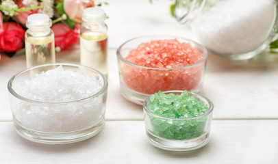 White, pink, green sea salt, two small glass bottles with liquid inside and rose flowers on a white wooden table