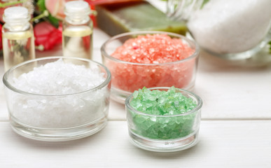 Three glass bowls with sea salt and other cosmetic items on a white wooden table