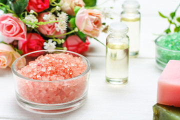 Red sea salt, two bottles with cosmetic oil and rose flowers on a white wooden table