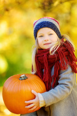Fototapeta premium Adorable little girl having fun on a pumpkin patch on beautiful autumn day
