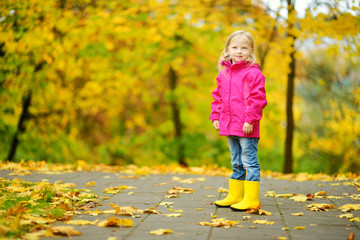 Cute little girl having fun on beautiful autumn day. Happy child playing in autumn park. Kid gathering yellow fall foliage.