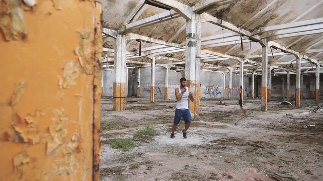 Male boxer doing shadow boxing exercise in an old abandoned building. Dolly shot.