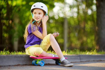 Pretty little girl learning to skateboard on beautiful summer day in a park. Child enjoying skateboarding ride outdoors.