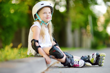 Pretty little girl learning to roller skate on beautiful summer day in a park