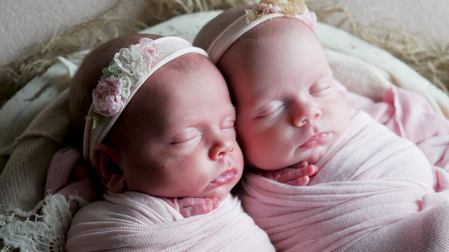 twin babies sleep in the crib in dresses and headband