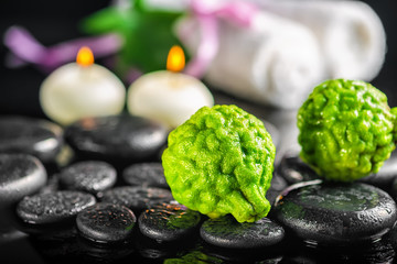 spa composition of bergamot fruits, leaf, candles, white towels and zen basalt stones with water drops on black background