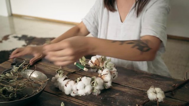 View of hipster millennial craftsman with artisan tattoos working on creating a floral decoration for wedding or party celebration, cotton florist art piece wreath for romantic beautiful bridal image