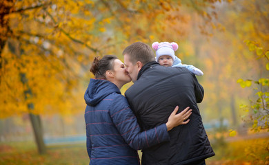 Fototapeta premium happy family walks in the autumn park, the father holds the kid on hands and kisses mother