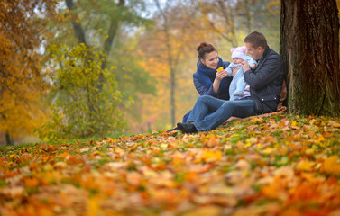 happy family walks in the autumn park, the father holds the kid on hands and considers the fallen-down leaves