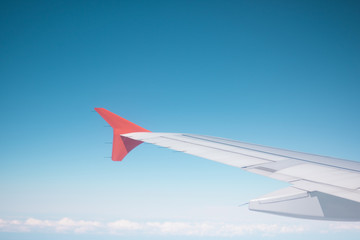 A wing of a plane is high in an air against a blue sky and above a horizon of white clouds. Concept: travel.