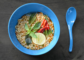 Instant noodles in blue bowl put on dark wood background, Top view, red spicy chili, lime and green vegetables, junk food concept