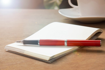 Open blank note papers and red pen on wood table with blur white coffee cup background, outdoor, garden vintage (retro) style color effect