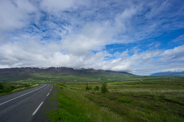 Iceland - Green moss covered volcanoes with snow covered tops behind road bend