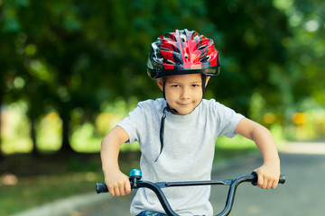 Naklejka premium Little boy learns to ride a bike in the Park near the home. Portrait of a cute kid on bicycle. Happy smiling child in helmet riding a cycling.