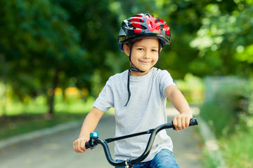 Little boy learns to ride a bike in the Park near the home. Portrait of a cute kid on bicycle. Happy smiling child in helmet riding a cycling.