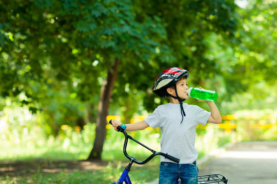 Little boy drinking water by the bike. Child in helmet riding a cycling.