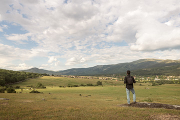 Mountain landscape with hiker with a backpack against the background of the mountain peaks, mountain pastures and the sky with clouds in spring day