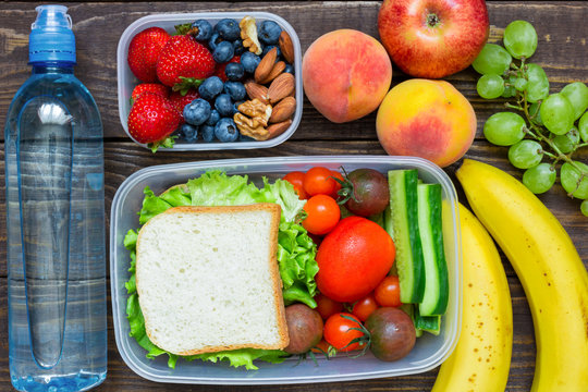 School lunch boxes with sandwich, fresh fruits and vegetables, berries and nuts and bottle of water