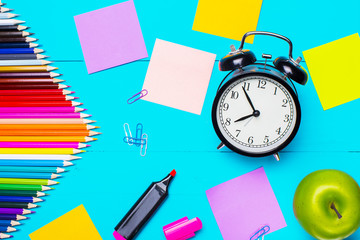 Stationery, alarm clock and apple on a blue wooden table