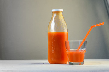 A bottle of carrot juice and a glass of carrot juice with a straw on white wood table. Still life of a healthy eating concept