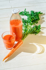 A bottle of carrot juice with with a stuffed glass and one fresh carrots on white wood table. Still life of a healthy eating concept