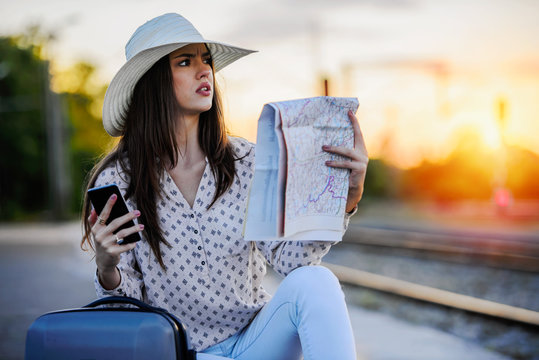 Lost young woman on train station with map and smart phone
