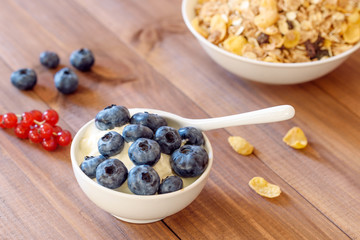 Bowl of breakfast healthy muesli with blueberry, red currant, cornflakes and yogurt.