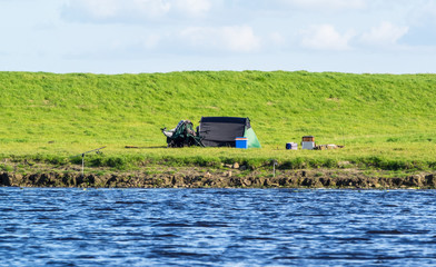 Fototapeta premium Angelstelle mit Angel und Zelt am Ufer von einem Fluss