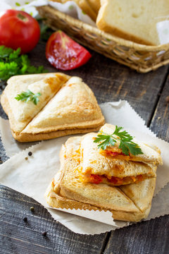 Pressed and toasted double sandwich with chicken, Korean carrots, cheese and tomatoes, served on a sandwich paper on a kitchen wooden table.