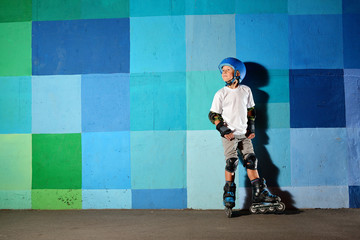 Cute little boy on roller skates standing against the blue graffiti wall
