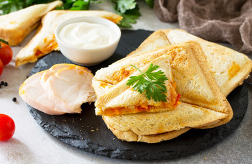 Pressed and toasted double sandwich with chicken, Korean carrots, cheese and tomatoes on a gray stone or slate.