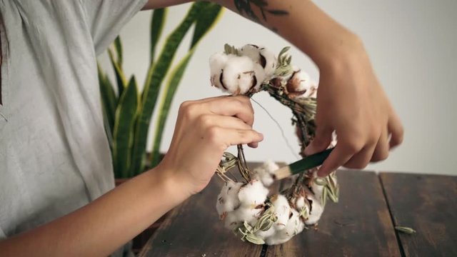 Florist woman hobby enthusiast learns how to create floral project from scratch after watching tutorials in floral workshop, weaves flowers, branches and blossoms together to create composition