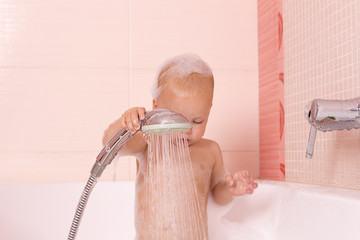 Adorable baby boy in a foam taking a douche, shower