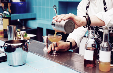 Bartender is pouring cocktail from shaker, toned