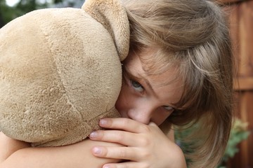 Little girl hugging teddy bear while looking intense
