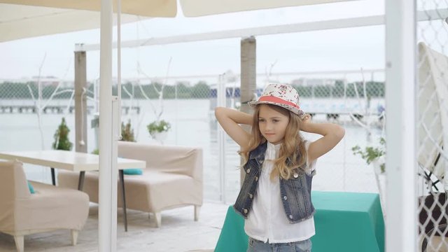Smart little female model in hat posing, looking and smiling at camera 4K