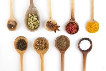DIVERSE ISOLATED SPICE ON WOODEN SPOON ON WHITE BACKGROUND. ANISE, GOJI, CARDAMOM, NUTMEG, CURRY, CORIANDER IN STILL LIFE