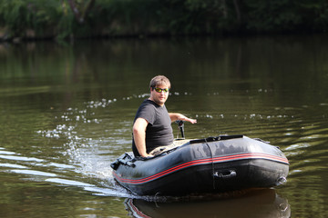 Junger Mann im Schlauchboot mit elektrischem Außenborder fährt am Fluss.