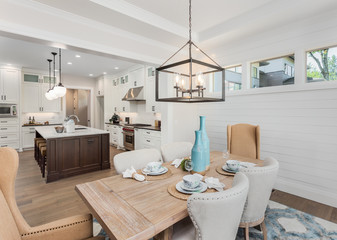 Dining Room and Kitchen Interior in New Luxury Home: Kitchen has Island, Sink, Cabinets, and Hardwood Floors. Dining Room has table with place settings. Pendant Lights accent Both Rooms