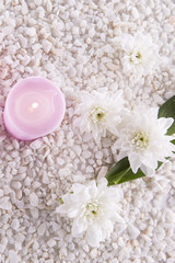 Spa. Still life. Candle, bottles with cream of pink color, a towel and flowers on a background of white pebbles. Top view
