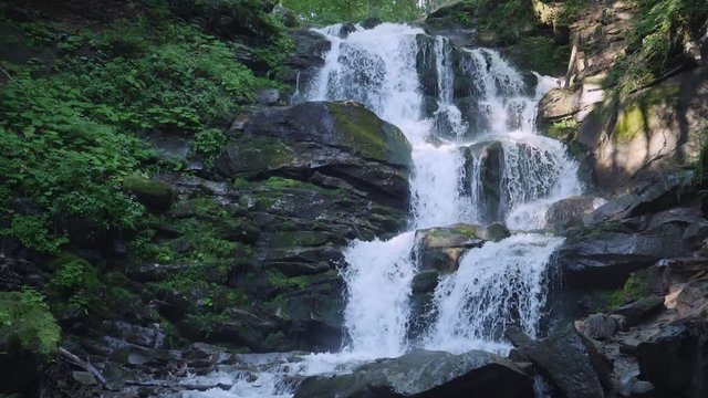 Amazing nature view on the waterfall surrounded by green plant and stones.