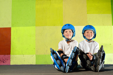 Yong little athletic boys on roller sitting against graffiti wall