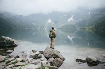 Young man standing on top of cliff in summer mountains at sunset