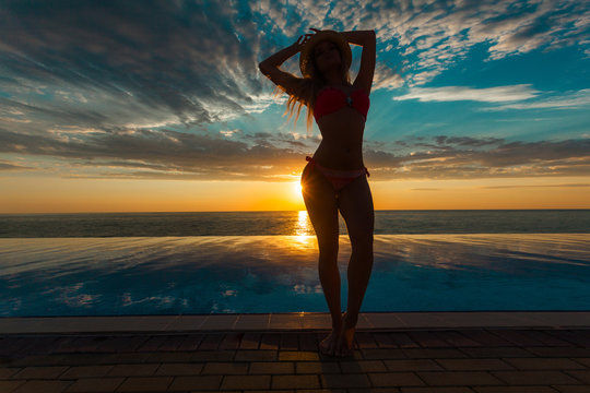Summer Vacation. Silhouette of beauty dancing woman on sunset near the pool with ocean view.