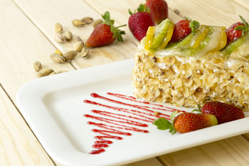 cream cake with strawberry kiwi and lemon on plate isolated on wooden background