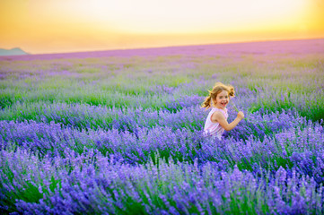 happy little girl plays and runs in the lavender field on a sunset