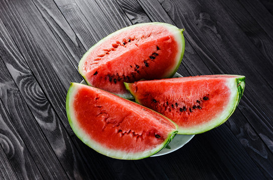 Background of three slices of a cut watermelon in a white plate on a black wooden table top view.
