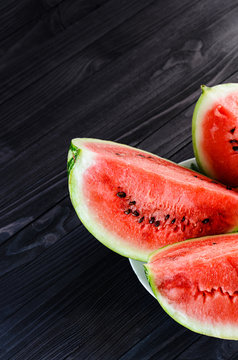 Background of three slices of a cut watermelon in a white plate on a black wooden table top view. Empty space for text